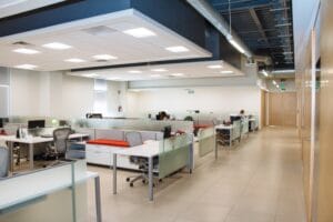 Empty open plan office with predominantly white and silver colour scheme and fluorescent lighting. There are no people present in the office